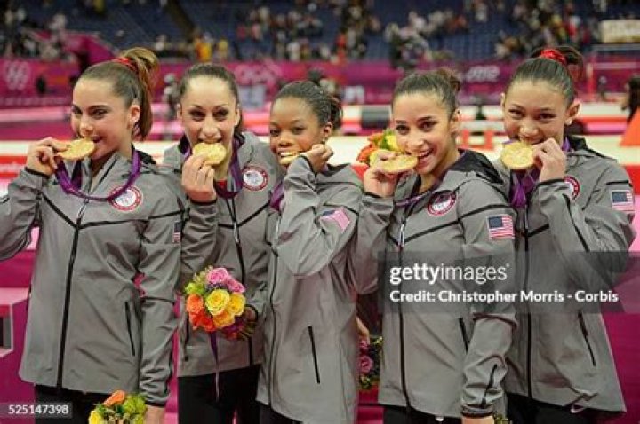 U.S. gymnasts, left to right wearing red, Gabrielle Douglas, McKayla Maroney, Alexandra Raisman, Jordyn Wieber and Kyla Ross celebrate with coaches Jenny Zhang, front left, Mihai Brestyan, back left, John Geddert, center, and Liang Chow, right, after their team won the gold medal for the Artistic Gymnastics women's team final at the 2012 Summer Olympics, Tuesday, July 31, 2012, in London. (AP Photo/Matt Dunham)